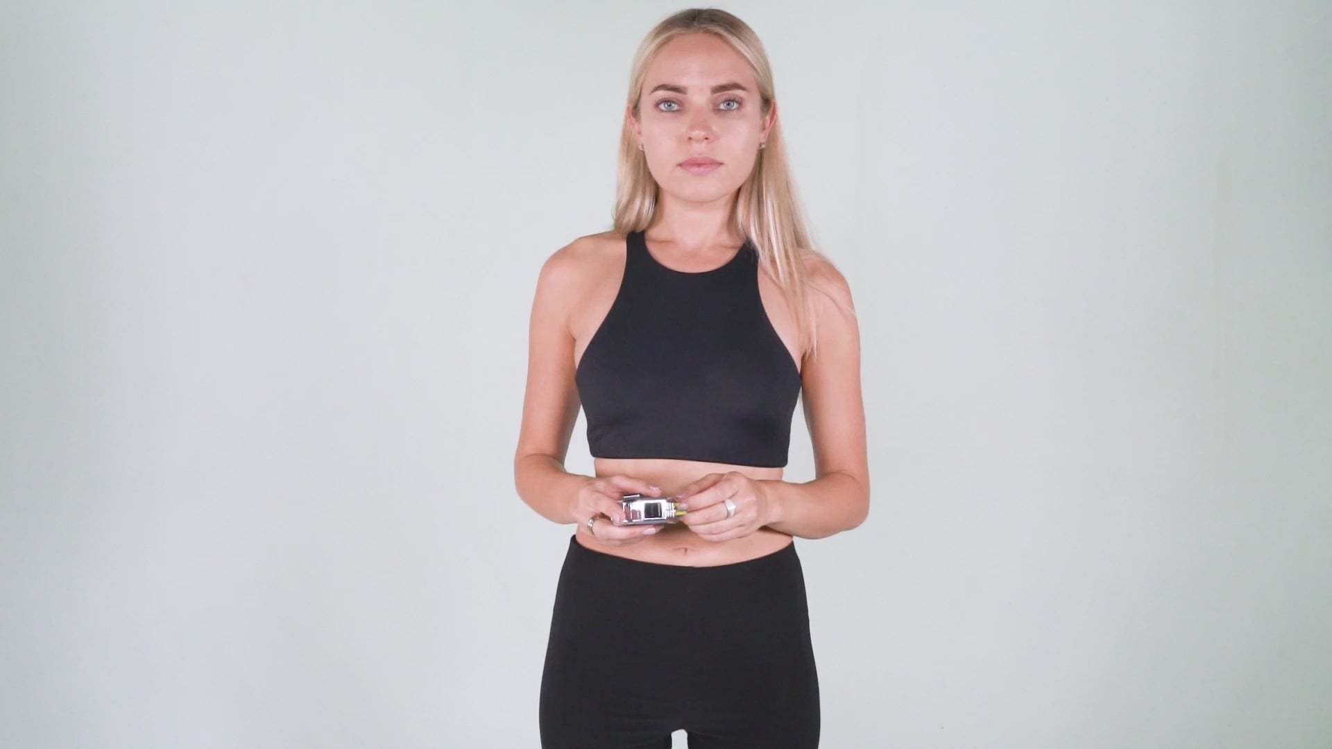 A woman wearing black athletic apparel on a white background holding a tape measure displaying how to measure your waist for proper Pumpcases fit.