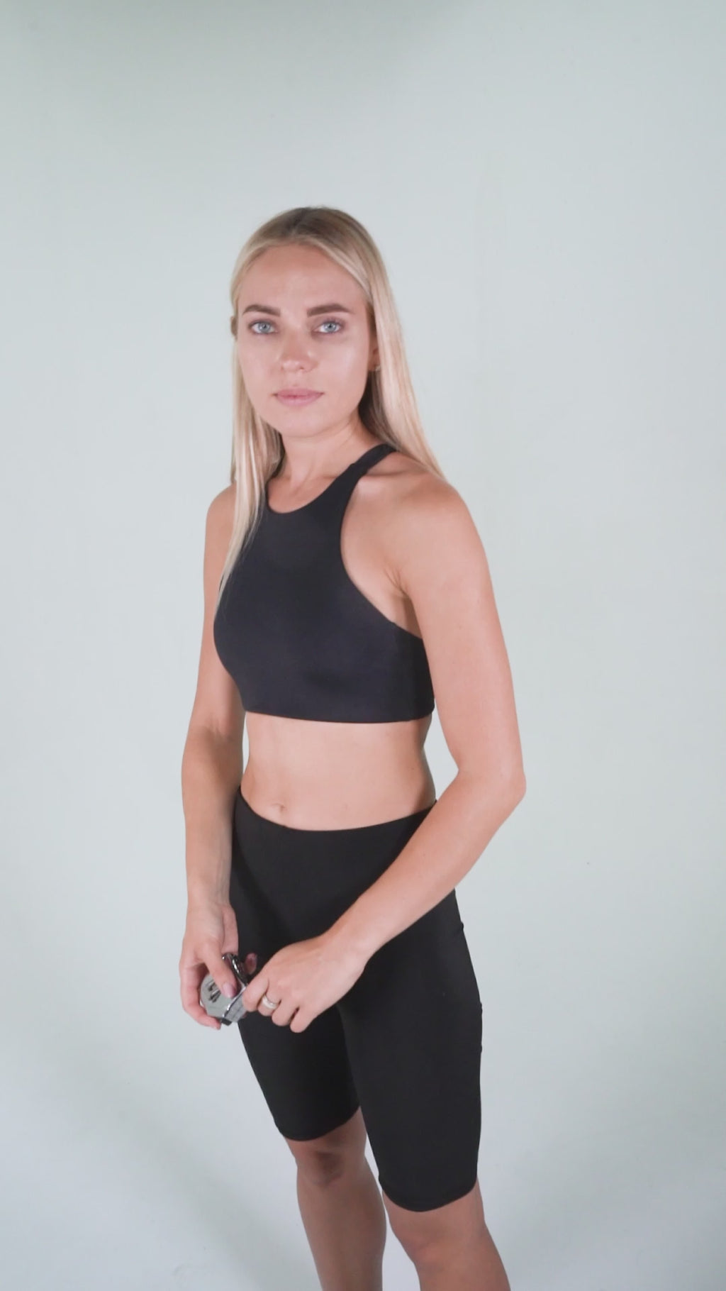A woman wearing black athletic apparel on a white background holding a tape measure displaying how to measure your arm for proper Pumpcases fit.