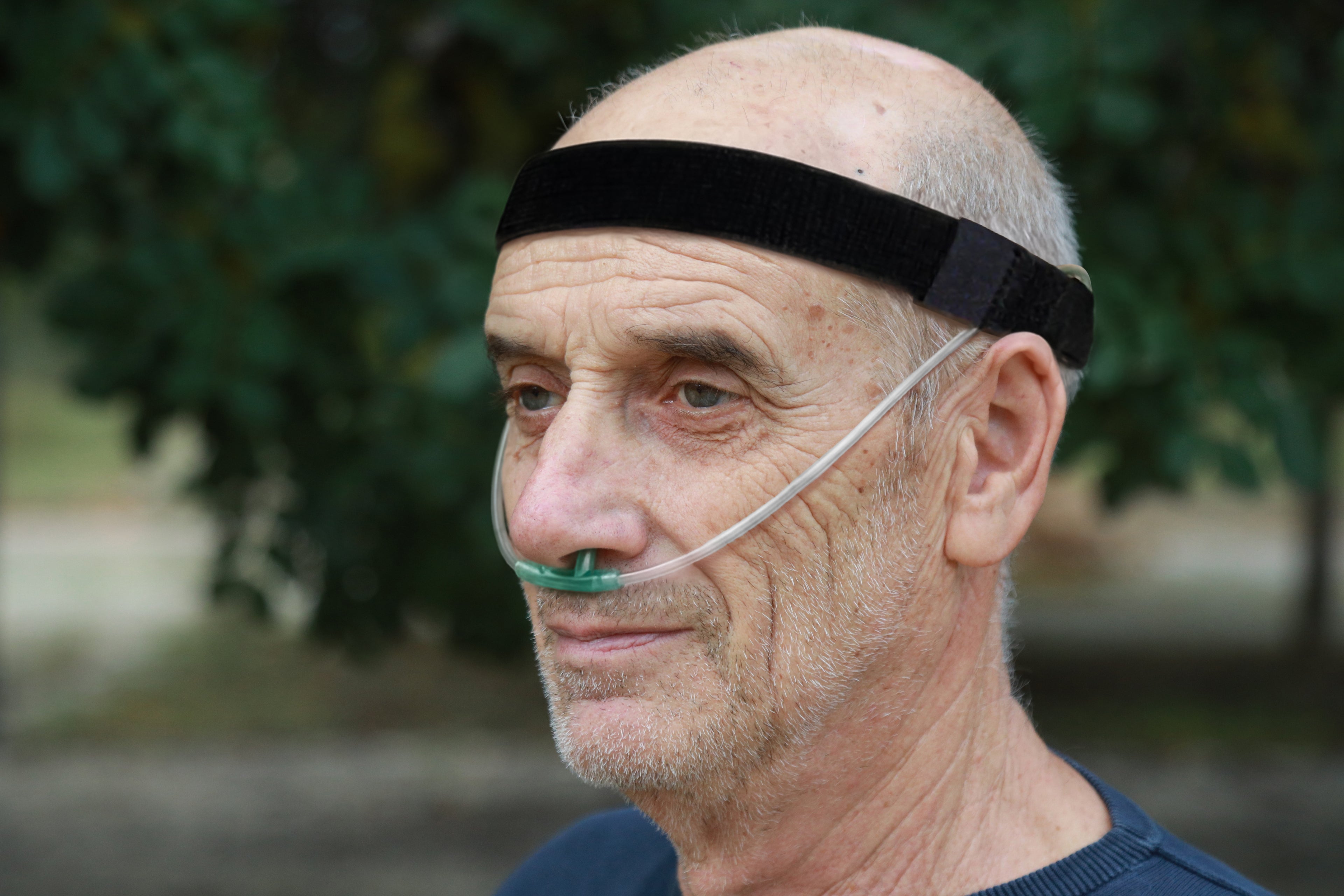 Man wearing a black headband with an oxygen tube in his nose outdoors.